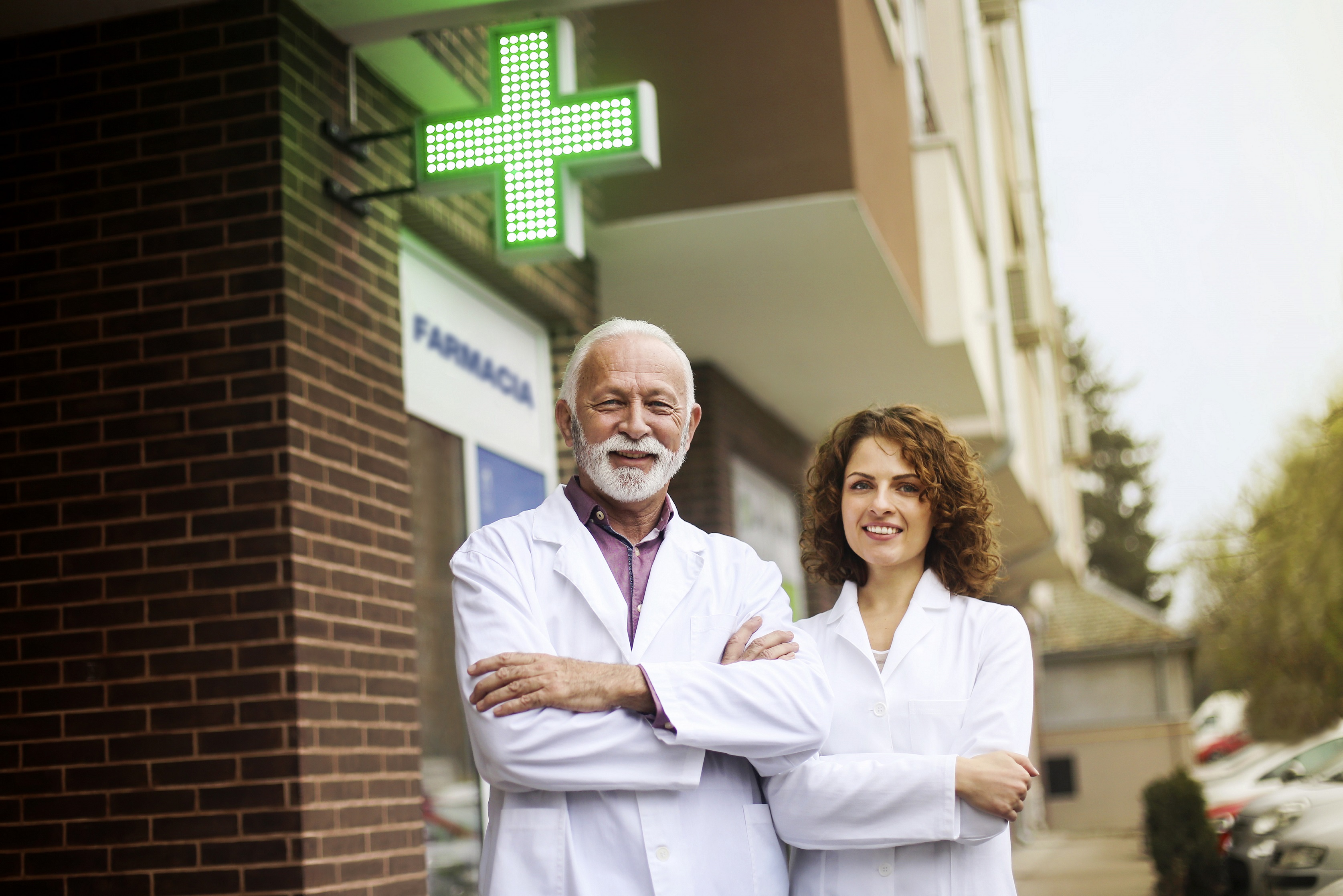 Young female and a senior male pharmacists in front of a pharmacy. About 25 and 65 years old, both Caucasian.